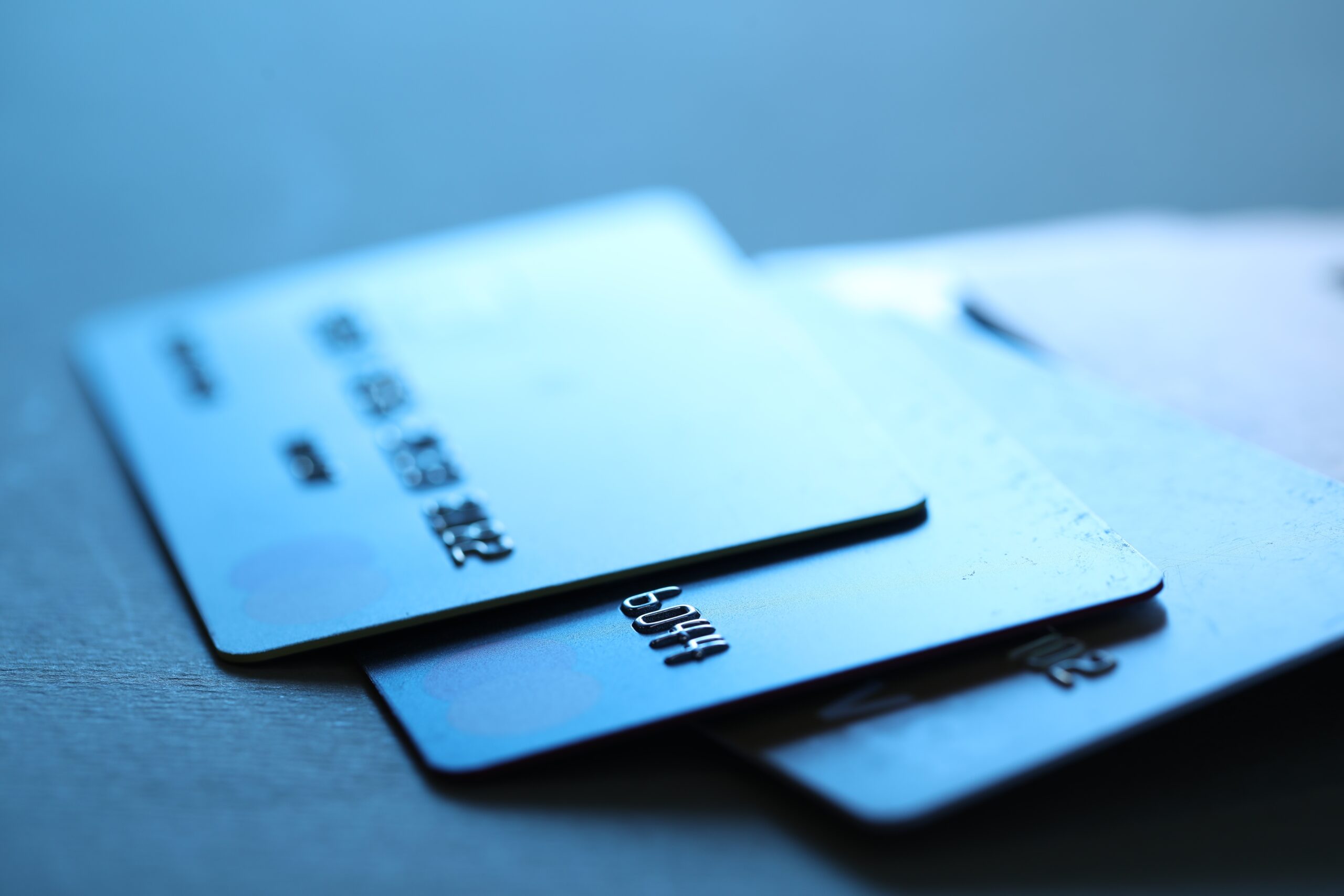 Two blue credit cards stacked on a wooden surface, blurred in the foreground and background lines.